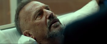 Movie still from “Criminal” (2016), directed by Ariel Vromen – A man with a beard is laying on a bed; Close Up shot, Over the shoulder angle