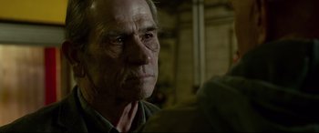 Movie still from “Criminal” (2016), directed by Ariel Vromen – An old man with a gray beard looking into the camera; Close Up shot, Over the shoulder angle