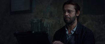 Movie still from “Criminal” (2016), directed by Ariel Vromen – A man with a goatee wearing glasses and a black jacket; Close Up shot, Over the shoulder angle
