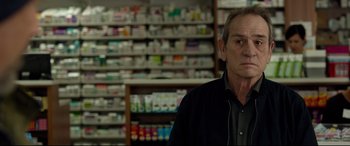Movie still from “Criminal” (2016), directed by Ariel Vromen – A man standing in front of a shelf filled with many different types of medicine; Close Up shot, Over the shoulder angle