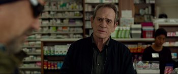 Movie still from “Criminal” (2016), directed by Ariel Vromen – An older man is standing in front of a pharmacy; Close Up shot, Over the shoulder angle