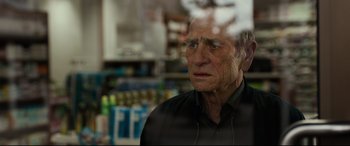 Movie still from “Criminal” (2016), directed by Ariel Vromen – An older man looking out of a store window; Close Up shot, Over the shoulder angle