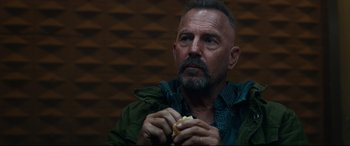 Movie still from “Criminal” (2016), directed by Ariel Vromen – A man holding a hot dog in his hands; Close Up shot, Over the shoulder angle