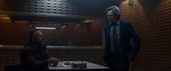 Movie still from “Criminal” (2016), directed by Ariel Vromen – A man standing in front of a table with food on top of it; Medium shot, Over the shoulder angle