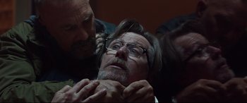 Movie still from “Criminal” (2016), directed by Ariel Vromen – A man with a beard and glasses is being held down by another man; Close Up shot, Low angle