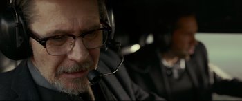 Movie still from “Criminal” (2016), directed by Ariel Vromen – An older man with glasses and a headset on; Close Up shot, Over the shoulder angle