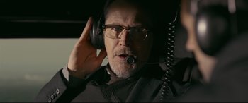 Movie still from “Criminal” (2016), directed by Ariel Vromen – An older man wearing glasses and holding a microphone; Close Up shot, Low angle