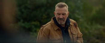 Movie still from “Criminal” (2016), directed by Ariel Vromen – An older man in a brown jacket is looking at the camera; Close Up shot, Over the shoulder angle