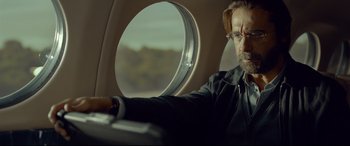 Movie still from “Criminal” (2016), directed by Ariel Vromen – A man with a beard and glasses sitting in a plane; Close Up shot, Over the shoulder angle