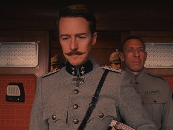 Movie still from “The Grand Budapest Hotel” (2014), directed by Wes Anderson – A man in a military uniform stands next to another man in a uniform; Close Up shot, Low angle