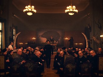 Movie still from “The Grand Budapest Hotel” (2014), directed by Wes Anderson – A group of people sitting in a room with candles; Wide shot, High angle