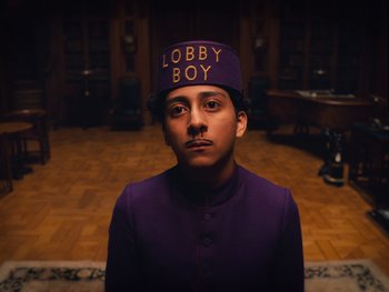 Movie still from “The Grand Budapest Hotel” (2014), directed by Wes Anderson – A man in a purple uniform and a purple hat; Medium shot, Low angle