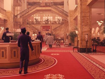 Movie still from “The Grand Budapest Hotel” (2014), directed by Wes Anderson – A man in a purple suit is walking through a lobby; Extreme Wide shot, High angle