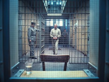 Movie still from “The Grand Budapest Hotel” (2014), directed by Wes Anderson – A man in a prison uniform standing in a jail cell; Wide shot, High angle