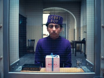 Movie still from “The Grand Budapest Hotel” (2014), directed by Wes Anderson – A man sitting at a table with a book on top of his head; Medium shot, Low angle