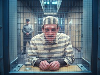 Movie still from “The Grand Budapest Hotel” (2014), directed by Wes Anderson – A man in a prison uniform sitting in a jail cell; Medium shot, High angle
