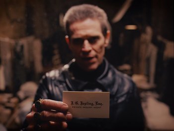 Movie still from “The Grand Budapest Hotel” (2014), directed by Wes Anderson – A man in a leather jacket holding up a business card; Close Up shot, Over the shoulder angle
