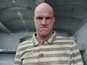 Movie still from “The Grand Budapest Hotel” (2014), directed by Wes Anderson – A bald man in a striped shirt is looking at the camera; Close Up shot, Low angle