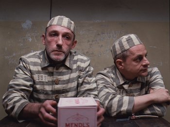 Movie still from “The Grand Budapest Hotel” (2014), directed by Wes Anderson – A couple of men sitting next to each other in prison uniforms; Medium shot, High angle