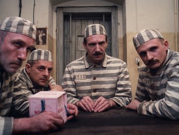 Movie still from “The Grand Budapest Hotel” (2014), directed by Wes Anderson – A group of men in striped uniforms sitting at a table; Medium shot, Low angle