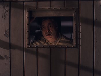 Movie still from “The Grand Budapest Hotel” (2014), directed by Wes Anderson – A man looking out of a window in a jail cell; Medium shot, High angle