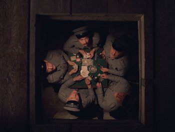 Movie still from “The Grand Budapest Hotel” (2014), directed by Wes Anderson – A group of men in uniform are sitting in a box; Wide shot, Overhead angle
