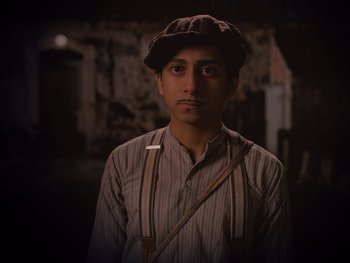 Movie still from “The Grand Budapest Hotel” (2014), directed by Wes Anderson – A man wearing a hat and suspenders in the dark; Close Up shot, Low angle