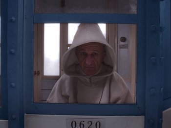 Movie still from “The Grand Budapest Hotel” (2014), directed by Wes Anderson – An old man wearing a hooded sweatshirt in a jail cell; Medium shot, Low angle