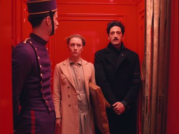Movie still from “The Grand Budapest Hotel” (2014), directed by Wes Anderson – A group of people standing next to each other in a room; Medium shot, Low angle