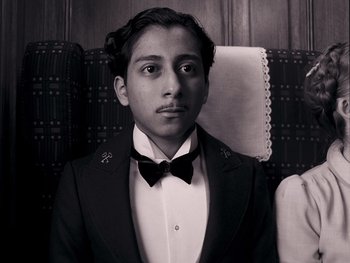 Movie still from “The Grand Budapest Hotel” (2014), directed by Wes Anderson – A man in a suit and bow tie sitting in a chair; Close Up shot, Overhead angle