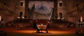 Movie still from “The Grand Budapest Hotel” (2014), directed by Wes Anderson – Two people are sitting at a table with a knife and a fork in their hands; Extreme Wide shot, Low angle