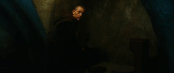 Movie still from “Crimson Rivers 2: Angels of the Apocalypse” (2004), directed by Olivier Dahan – A man standing in a dark room with a book in front of him; Medium shot, Low angle