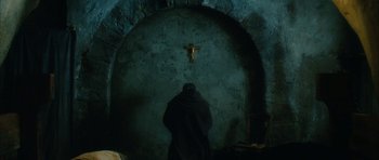 Movie still from “Crimson Rivers 2: Angels of the Apocalypse” (2004), directed by Olivier Dahan – A person standing in front of a wall with a crucifixion; Wide shot, Low angle