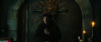 Movie still from “Crimson Rivers 2: Angels of the Apocalypse” (2004), directed by Olivier Dahan – A man holding a drink in front of a cross; Medium shot, Low angle