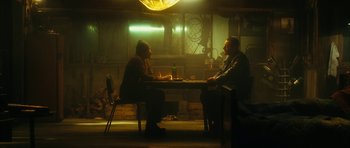Movie still from “Crimson Rivers 2: Angels of the Apocalypse” (2004), directed by Olivier Dahan – Two men sitting at a table in a dimly - lit room; Wide shot, Low angle