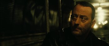 Movie still from “Crimson Rivers 2: Angels of the Apocalypse” (2004), directed by Olivier Dahan – A man in a leather jacket sitting in front of a metal fence; Close Up shot, Over the shoulder angle