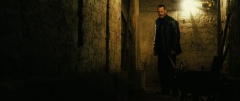 Movie still from “Crimson Rivers 2: Angels of the Apocalypse” (2004), directed by Olivier Dahan – A man standing in the dark in front of a brick wall; Medium shot, Low angle