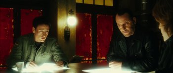 Movie still from “Crimson Rivers 2: Angels of the Apocalypse” (2004), directed by Olivier Dahan – Two men sitting at a table in front of a wall; Medium shot, Over the shoulder angle