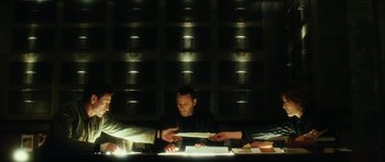 Movie still from “Crimson Rivers 2: Angels of the Apocalypse” (2004), directed by Olivier Dahan – A man sitting at a table in front of a book; Medium shot, Low angle