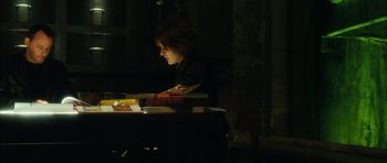 Movie still from “Crimson Rivers 2: Angels of the Apocalypse” (2004), directed by Olivier Dahan – A person sitting at a table with a stack of books; Medium shot, High angle
