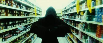 Movie still from “Crimson Rivers 2: Angels of the Apocalypse” (2004), directed by Olivier Dahan – A person in a hooded jacket in front of shelves of food; Medium shot, Low angle