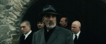 Movie still from “Crimson Rivers 2: Angels of the Apocalypse” (2004), directed by Olivier Dahan – An older man in a suit and a hat; Medium shot, Low angle