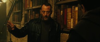 Movie still from “Crimson Rivers 2: Angels of the Apocalypse” (2004), directed by Olivier Dahan – A man wearing a leather jacket in front of some books; Medium shot, Over the shoulder angle