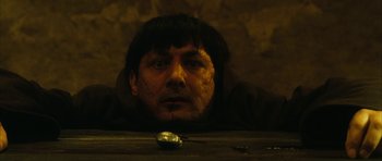 Movie still from “Crimson Rivers 2: Angels of the Apocalypse” (2004), directed by Olivier Dahan – A man is looking at the camera while sitting on a table; Close Up shot, Overhead angle