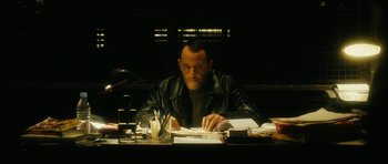 Movie still from “Crimson Rivers 2: Angels of the Apocalypse” (2004), directed by Olivier Dahan – A man sitting at a desk writing on a piece of paper; Medium shot, High angle