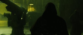 Movie still from “Crimson Rivers 2: Angels of the Apocalypse” (2004), directed by Olivier Dahan – A person in a hooded cloak standing in the dark; Medium shot, Over the shoulder angle