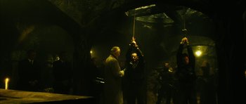 Movie still from “Crimson Rivers 2: Angels of the Apocalypse” (2004), directed by Olivier Dahan – A man holding up a stick while standing next to another man; Wide shot, Low angle
