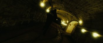 Movie still from “Crimson Rivers 2: Angels of the Apocalypse” (2004), directed by Olivier Dahan – A man is standing in a dark tunnel with lights on; Extreme Wide shot, Low angle