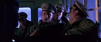 Movie still from “Crimson Tide” (1995), directed by Tony Scott – A group of men in military uniforms on a train; Medium shot, Over the shoulder angle