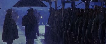 Movie still from “Crimson Tide” (1995), directed by Tony Scott – A group of people standing in the rain under umbrellas; Wide shot, Over the shoulder angle
